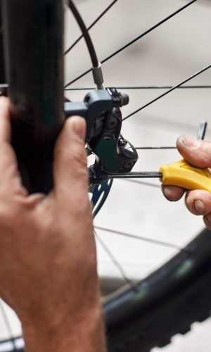 Cropped shot of male mechanic working in bicycle repair shop, serviceman repairing bike brakes using special tool