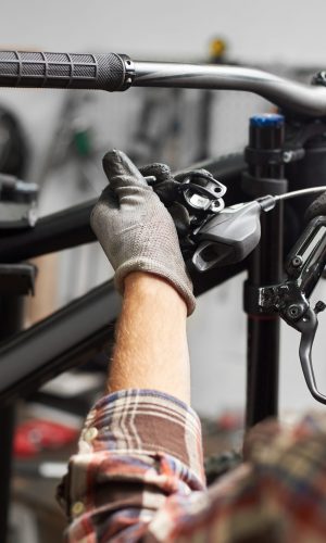 Cropped shot of professional repairman working in bicycle repair shop, mechanic repairing bike using special tool, wearing protective gloves
